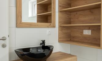 A modern bathroom with a wooden shelf and a black sink. On the wall, there are wooden shelves and a rectangular mirror.