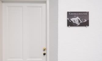 A white door with a golden doorknob. Next to the door hangs a sign with the inscription "GROßGLOCKNER" and an image of mountains.