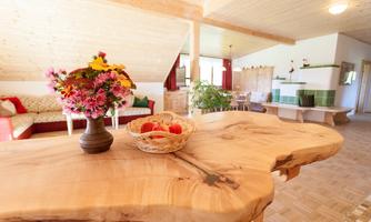 An inviting living room with a large wooden table. On the table, there is a vase of flowers and a basket of apples.