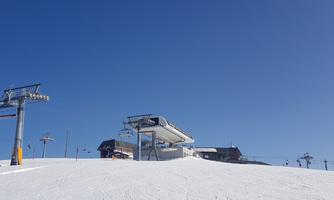 A ski resort with chairlifts and plenty of snow. The sky is clear and blue.
