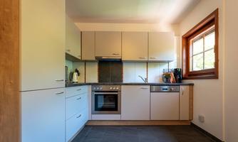 A modern kitchen with a bright cabinet design and a window that lets in daylight. The kitchen area is functionally equipped with a stove, a sink, and a coffee machine.