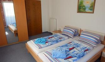 A bright bedroom with two single beds and colorful bedding. A large mirror and a painting on the wall complete the room.