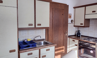 A bright kitchen with white and brown cabinets. A sink, a stove, and a window are visible.
