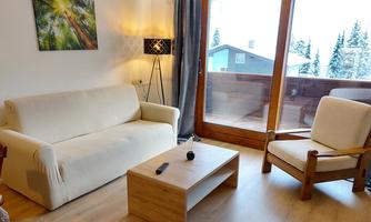A cozy living room with a white sofa and a wooden coffee table. Large windows offer a view of the winter landscape.