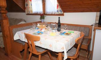 A cozy dining area with a table set for a meal. The room has wooden walls and windows with curtains.
