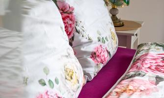 Comfortable bed with floral bedding and a deep berry-colored topper, along with a decorative table lamp. A cozy retreat after a day of exciting vacation activities.