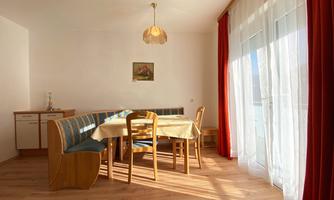A bright dining area with a table and chairs. Large windows let in plenty of light and offer a pleasant view.
