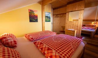 A cozy bedroom with a double bed that has red-and-white checkered bedding. The walls are painted in a warm yellow tone, and there are wood paneling and some pictures.