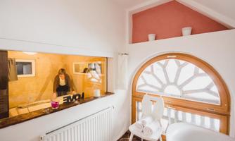 A cozy room with a large window and an elegant curve. In the background, a person can be seen working at a table.