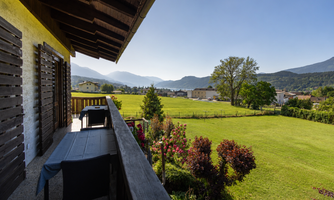 A beautiful balcony with a view of green meadows and mountains. The sun is shining and the sky is clear.
