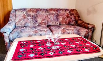 A living room with a patterned sofa and a table with a red tablecloth. On the table, there are two glasses.
