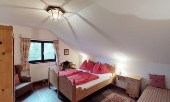A cozy bedroom with two beds and red-covered pillows. The room features a warm wood design and a window with a view outside.