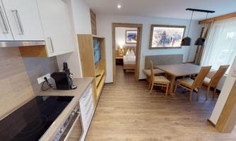 A modern kitchen with wooden shelves and a dining area. The room is bright and cheerfully designed.