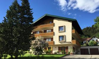 A beautiful house with a balcony and green surroundings. The clear blue sky and the trees give the scene an inviting atmosphere.