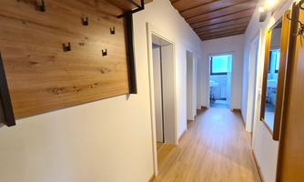 A bright hallway with a wooden panel for a coat rack and several doors. The floor is made of light wood and the walls are painted bright.
