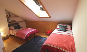 A cozy bedroom with two beds and red-and-white bedding. The room has a window that lets in daylight.
