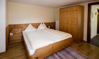A cozy bedroom with a wooden double bed and two pillows. The walls are bright, and the decor is simple, creating a relaxed atmosphere.