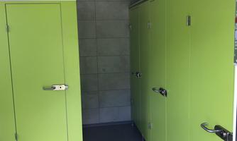 A modern changing room with green cubicles. The walls are made of gray material and the floor is dark.