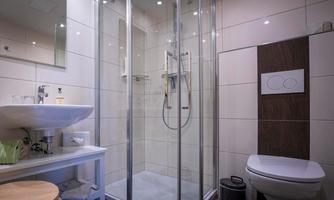 A modern bathroom with a glass shower and a sink. Next to the shower, there is a toilet and a small table.