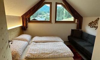A cozy bedroom in the attic with a double bed and a sofa. Large windows provide a view of the mountains.