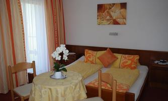 A cozy room with a double bed and a small table. The walls are decorated with orange curtains and a decorative mural.