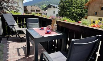 An inviting balcony with a table and chairs. In the background, you can see green mountains and a quiet residential area.