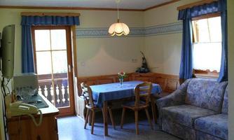 A cozy living area with a dining table and chairs. The windows have blue curtains and provide access to a balcony.