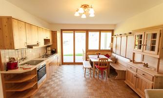 A modern kitchen with wooden cabinets and a large window. There is a dining table with chairs and a view of the garden.