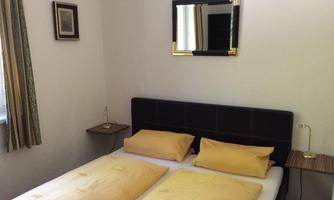 A simple bedroom with a double bed and yellow pillows. A mirror hangs on the wall, and there are nightstands with lamps.