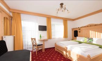 A cozy hotel room with two beds and a table. The walls are light, and there are large windows with yellow curtains.
