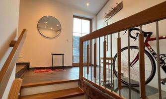 A bright entrance area with a wooden staircase and modern light sources. A bicycle stands by the railing, and a round mirror hangs on the wall.