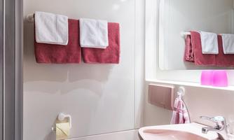 A modern bathroom with a pink sanitary installation. There are red towels and a large mirror above the sink.