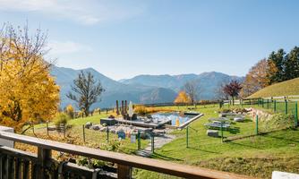 A picturesque view of a green landscape with a pool and mountains in the background. Colorful trees add an autumnal charm to the scene.