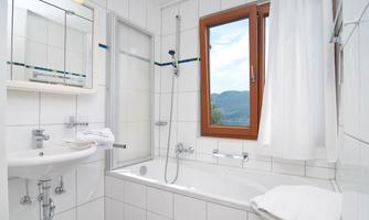 A modern bathroom with a bathtub and a sink. A window offers a view of the mountains.