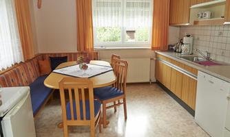 A cozy kitchen with a round table and a corner bench. The walls are decorated with orange curtains, and the appliances are modern.