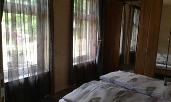 A cozy bedroom with two beds. Large windows with curtains let in a lot of light.