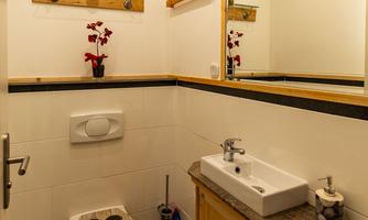 A modern bathroom with a stylish toilet area and a wooden countertop. The space is designed to be bright and friendly, featuring elegant mirror lighting.