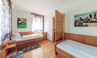 A cozy room with two single beds and wooden paneling. A window lets in plenty of daylight, and there are decorative pictures on the walls.