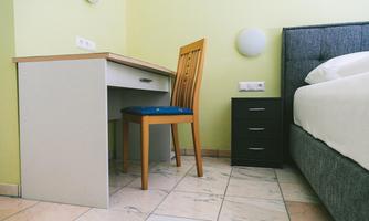 A simple room with a desk and a chair. Next to the bed is a nightstand.