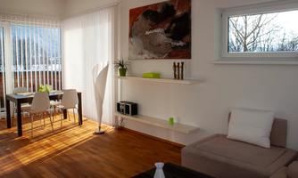 A modern living room with a bright, cozy ambiance. There is a comfortable couch, a dining table, and decorative elements on the wall.
