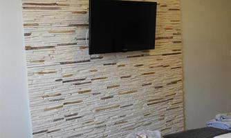 A modern bedroom with a television on a decorative stone wall. The bed is neatly decorated with fresh towels.