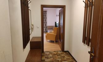A hallway with wooden furniture and coat hooks. In the background, a cozy living room with an orange armchair is visible.