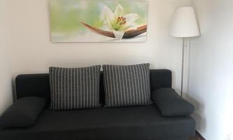 A modern seating area with a gray sofa and striped cushions. Next to the sofa is a small table with a remote control and a lamp.