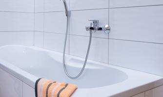 A modern bathtub with a shower fixture. An orange towel is lying on the edge of the tub.
