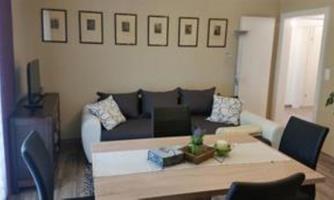 A modern living room with a comfortable sofa and a large table. Framed pictures hang on the wall, and the room has a bright, inviting atmosphere.