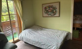 A simple bedroom with a bed and a window that looks out to nature. A flower picture hangs on the wall.