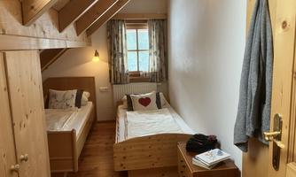 A cozy bedroom with two beds and wooden paneling. A window lets in natural light, and a small dresser is positioned next to the beds.