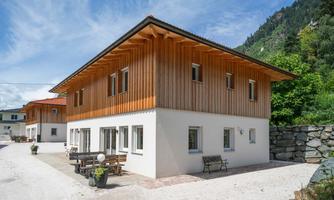 A modern house with wooden cladding and large windows. The surroundings are green and mountainous, ideal for peace and relaxation.