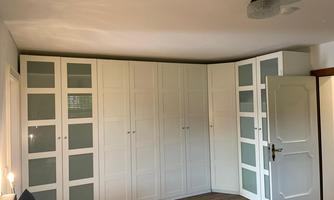 A modern room with a large, white built-in closet. The closet has glass doors and is positioned in a corner of the room.