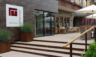 A modern building with a terrace and plenty of outdoor seating. A large sign reading "MOSER HOF" is clearly visible.